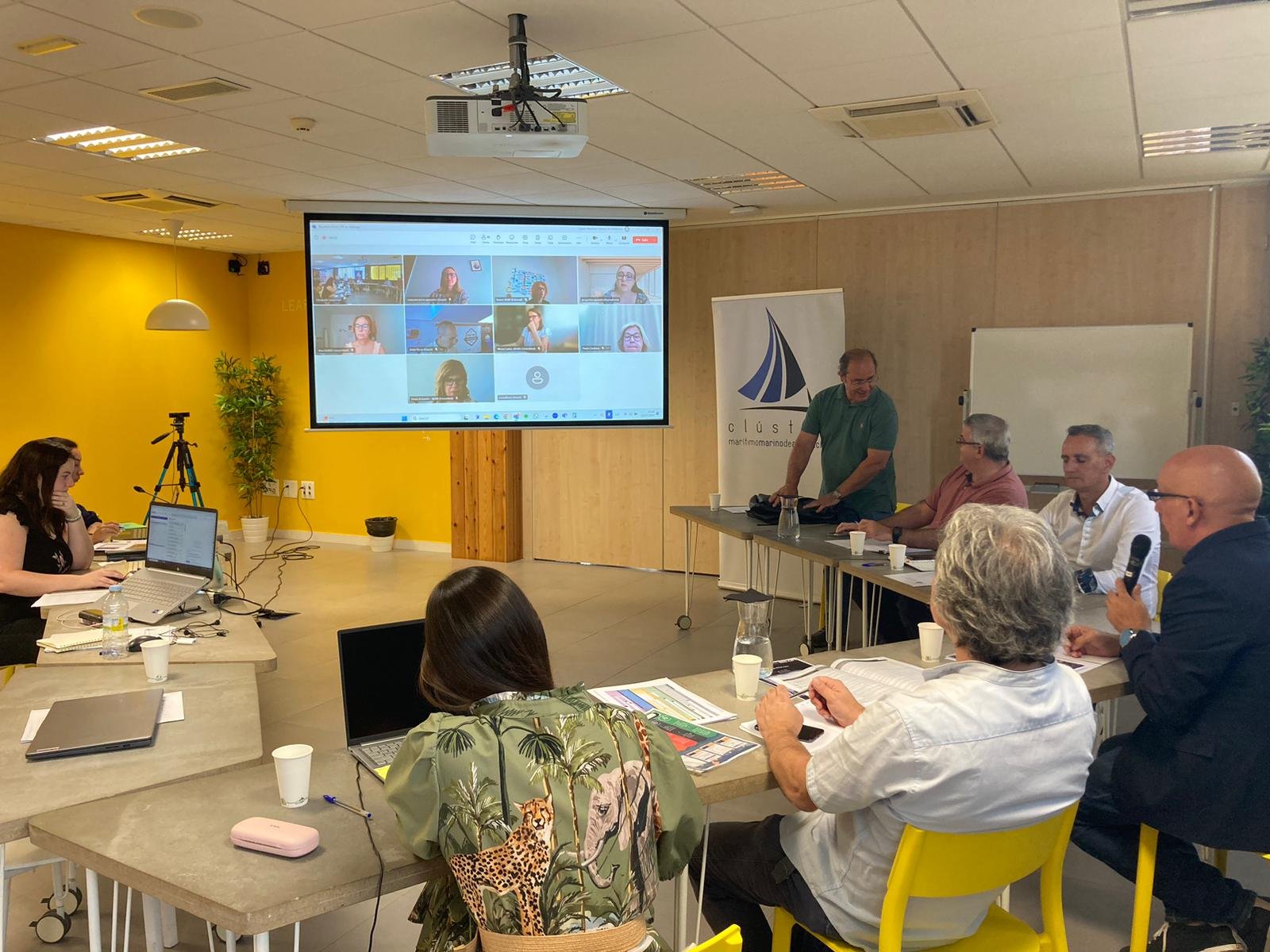 Imagem da reunião de lançamento do projeto, com alguns dos membros da parceria sentados diante uma tela que projeta os outros participantes numa reunião em videoconferência